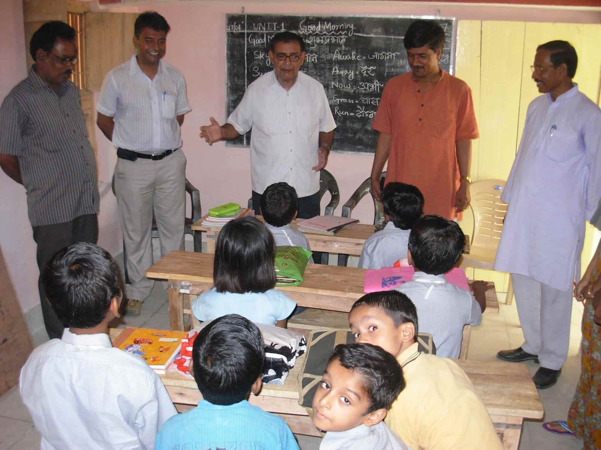 Classroom session with children at desks and trustees observing