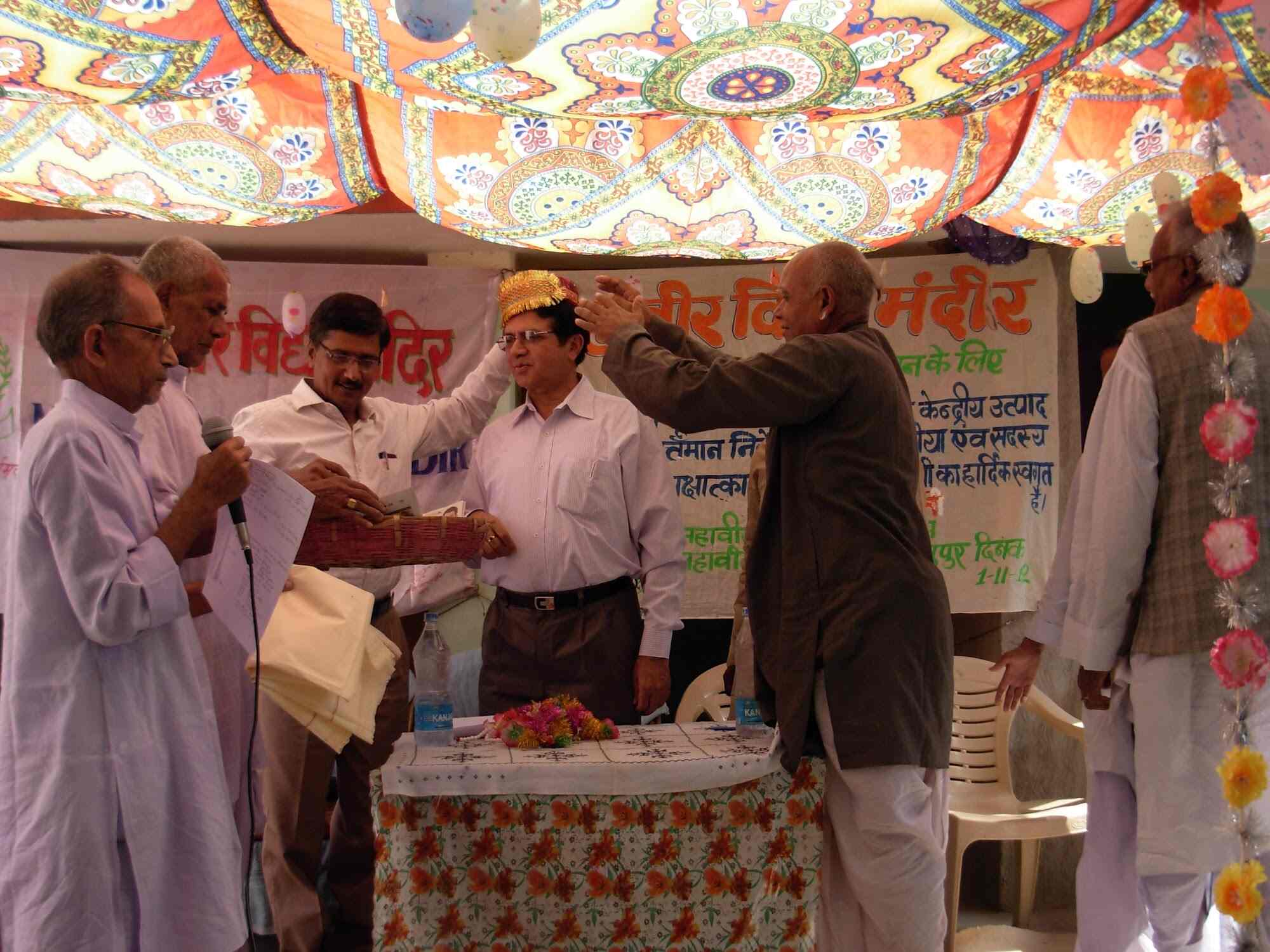 Felicitation ceremony with Trust members garlanding a guest under a marquee