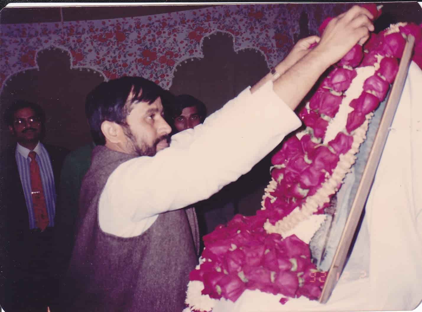 Second view of garlanding ceremony with Trust member adjusting a garland on Mahavir Singh's framed portrait