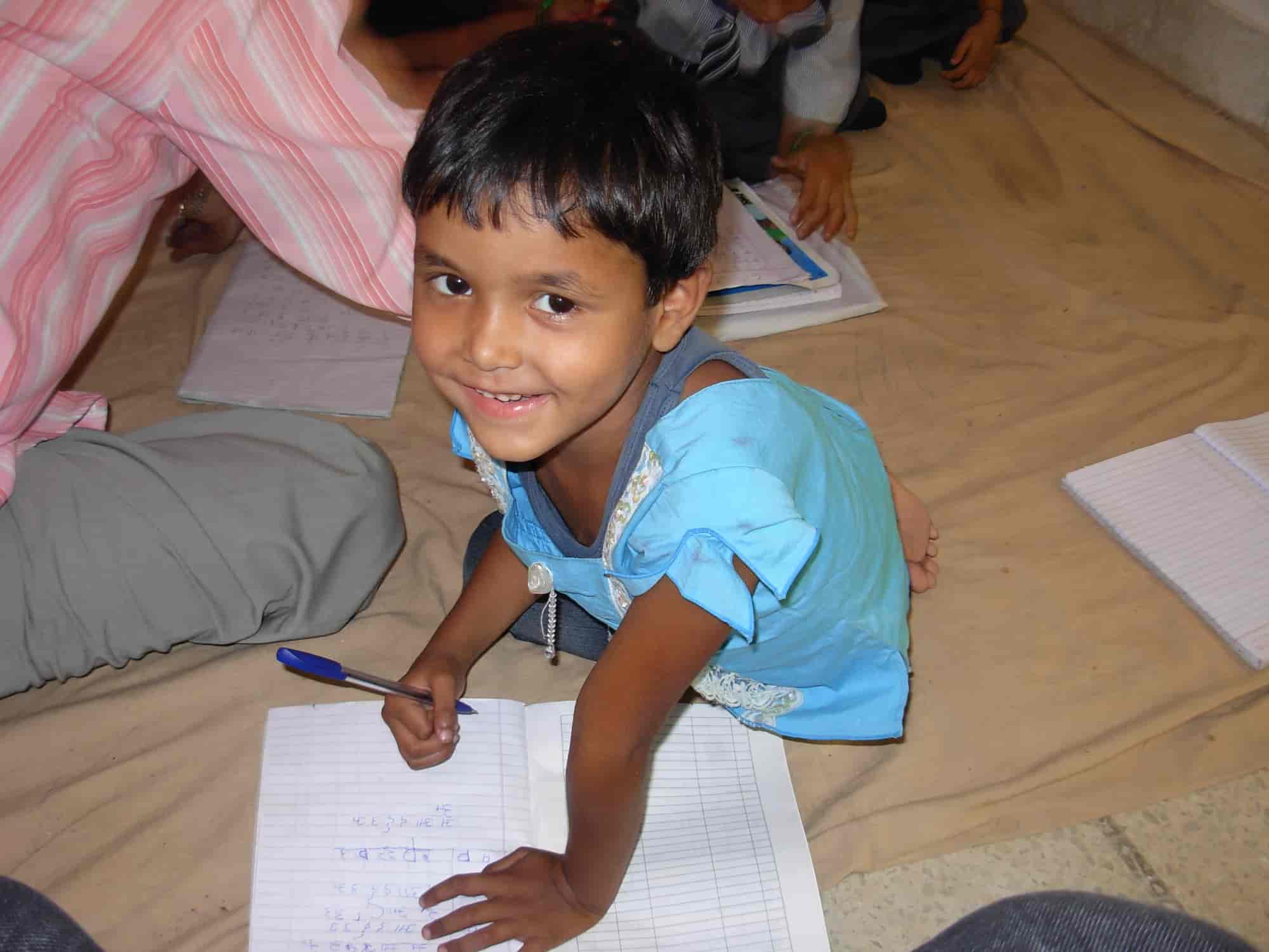 Close-up of a young girl student writing Hindi letters in a notebook on the classroom floor