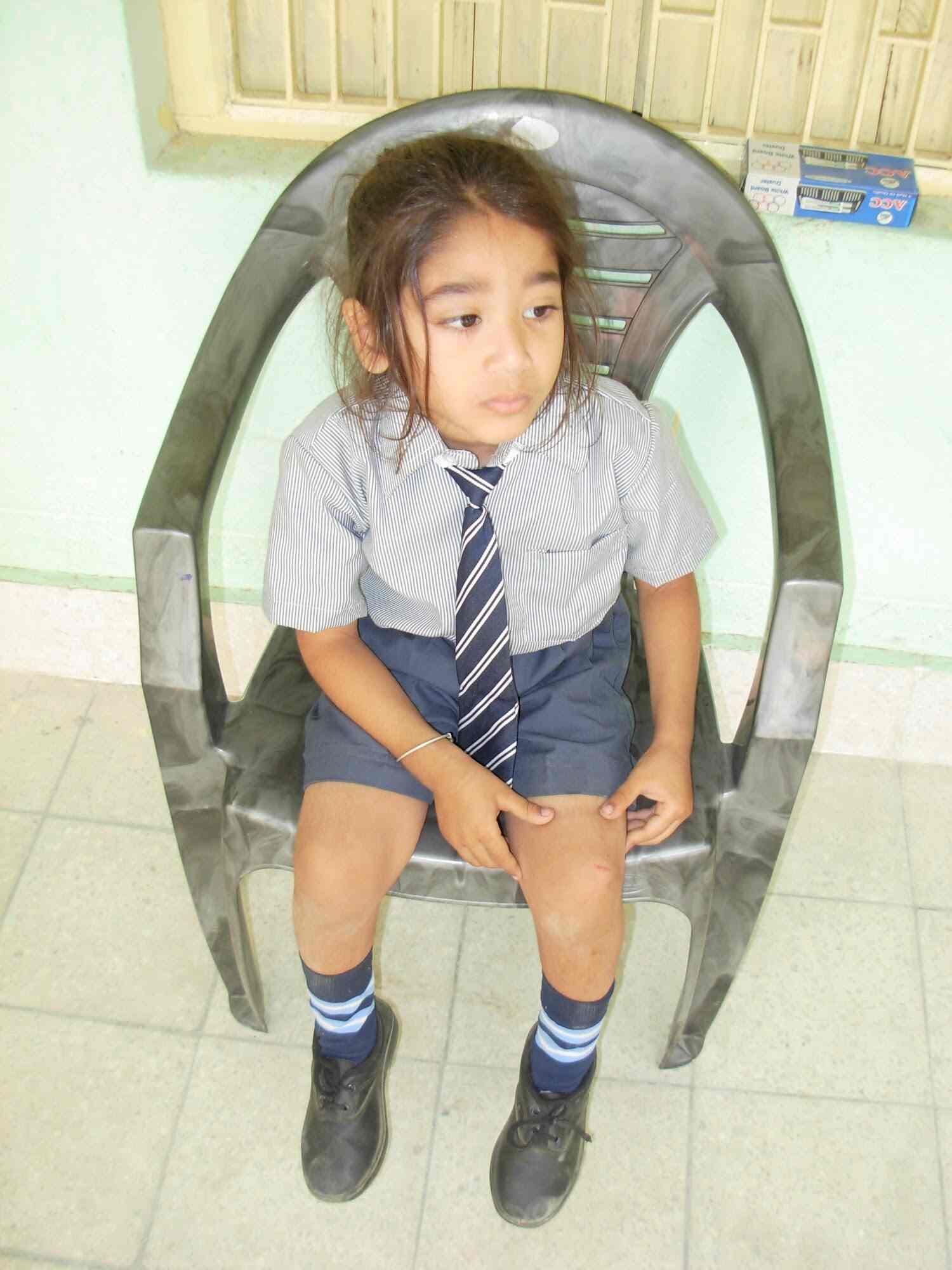 Portrait of a young girl student in striped school uniform sitting in a plastic chair