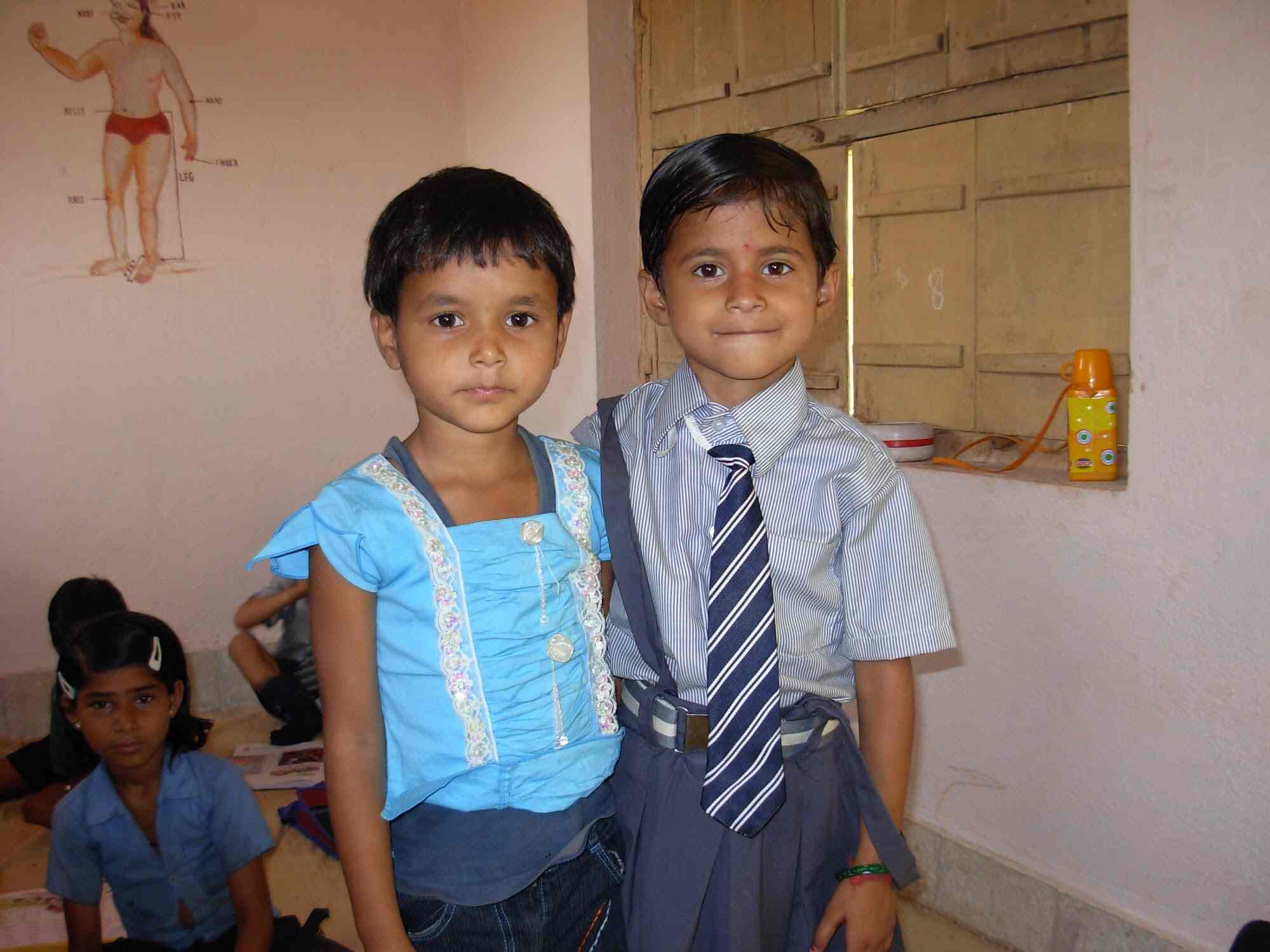 A girl in a blue dress and a boy in striped shirt and tie standing together in the classroom