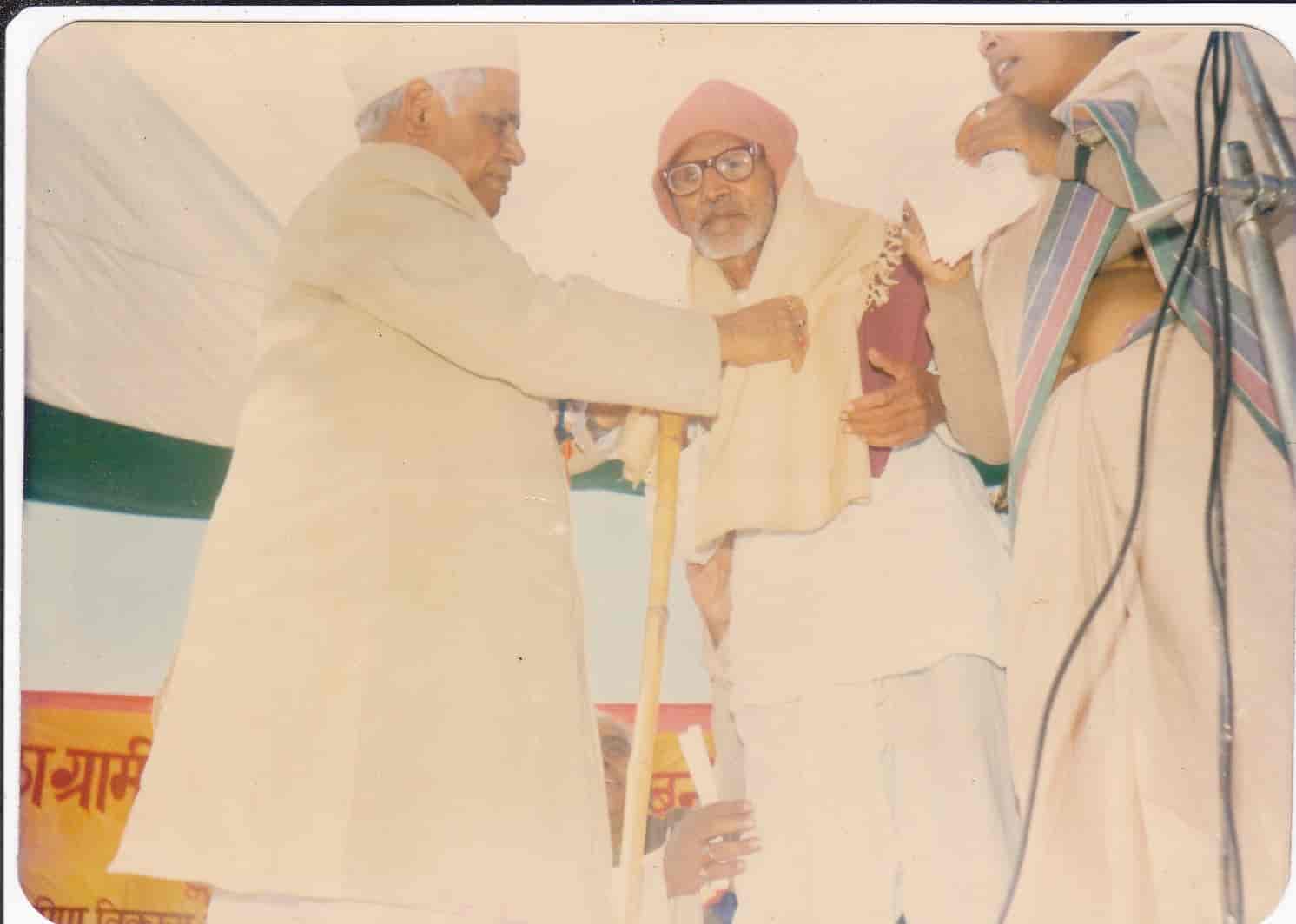 Elderly freedom fighter being honored with a shawl by a dignitary at a public function, sepia-toned archival photograph